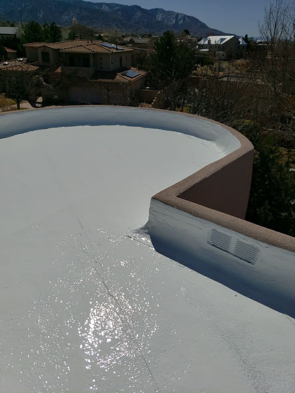 A finished coated flat roof with a New Mexico mountain view, the kind pictured in a Paramount Roofing Roof Health Report