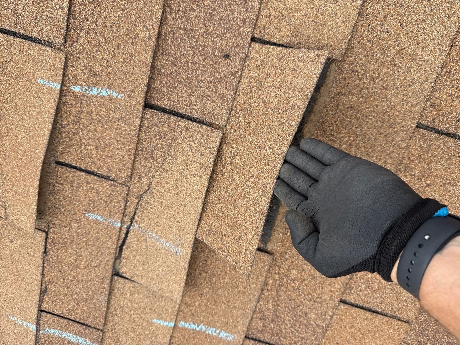 A Paramount Roofing inspector lifting and examining shingles by hand during a roof inspection in New Mexico