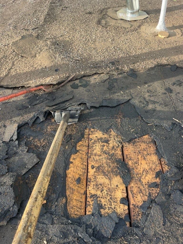 Exposed rotted wood roof decking revealed under a failing roof surface
