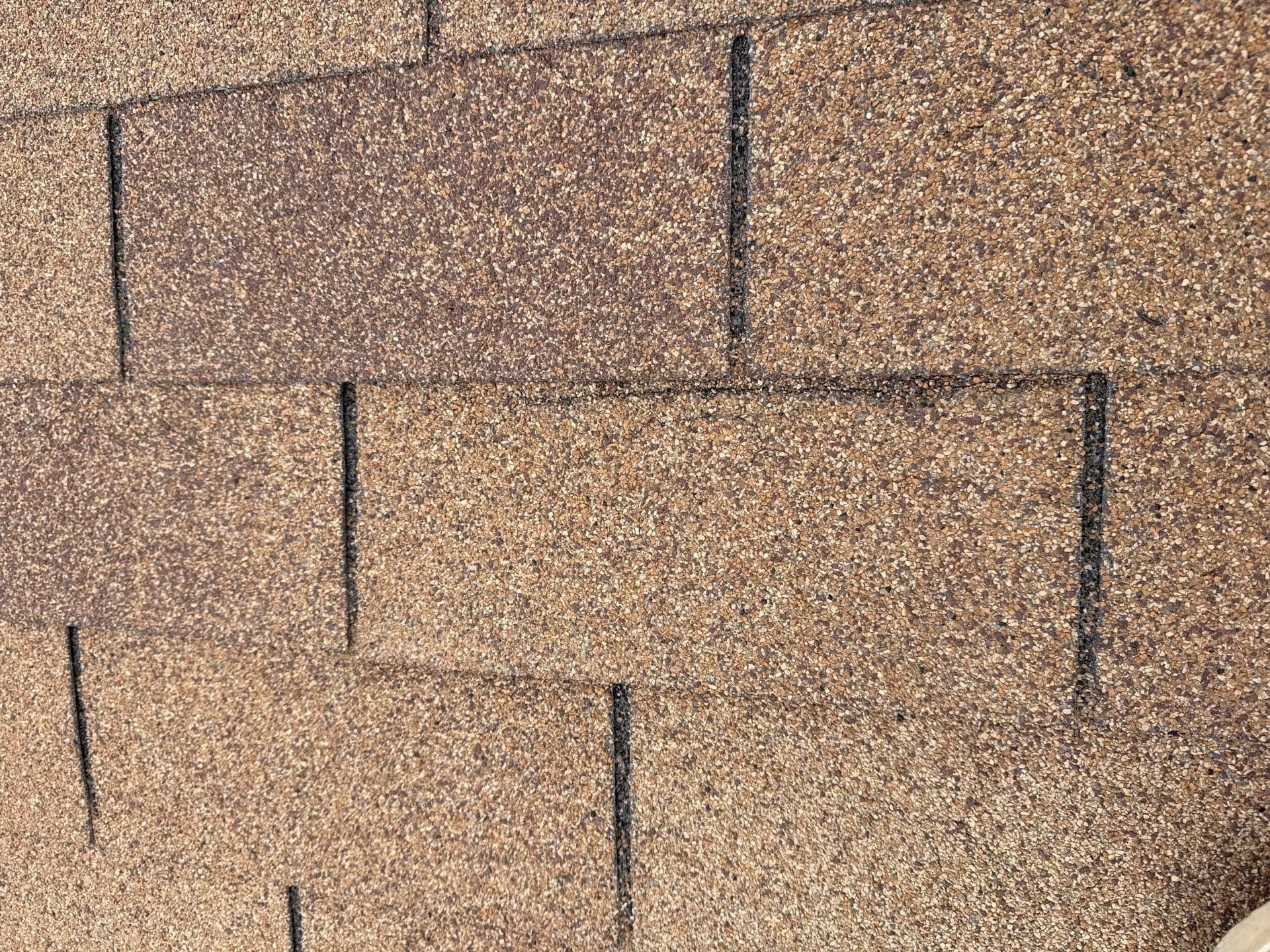 Close-up of an asphalt shingle roof with granule loss exposing the asphalt underneath