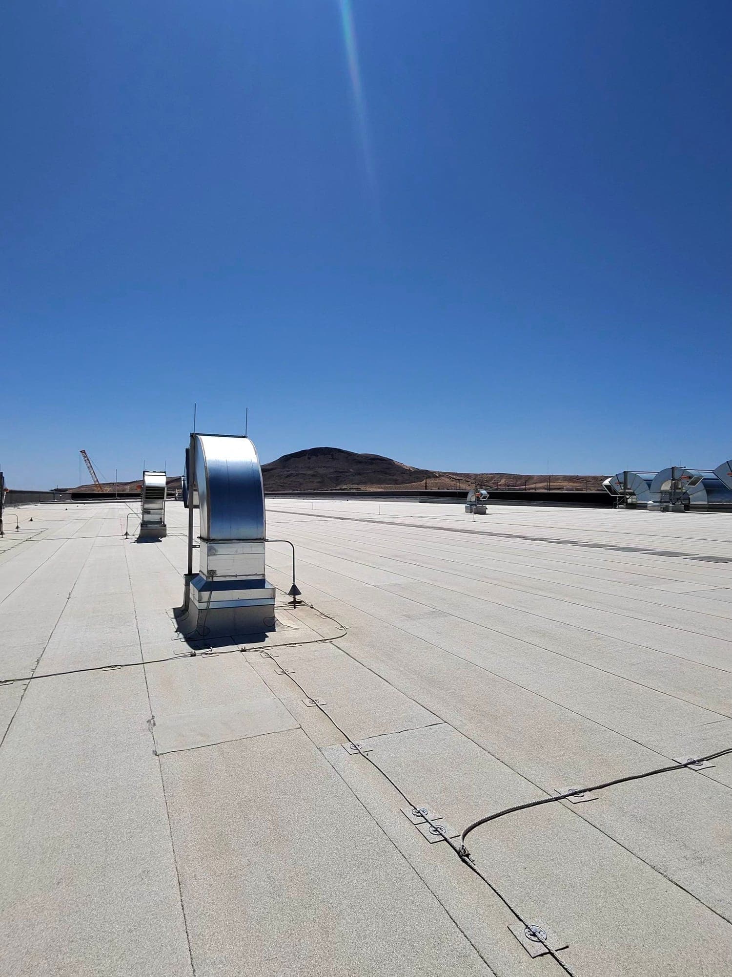 A flat commercial roof with rooftop ductwork stretching toward the New Mexico desert hills, maintained by Paramount Roofing