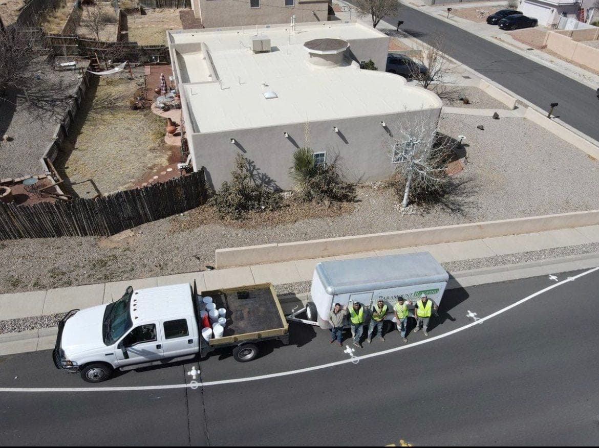 Aerial view of the Paramount Roofing crew with their branded truck and trailer in front of a flat-roof New Mexico home