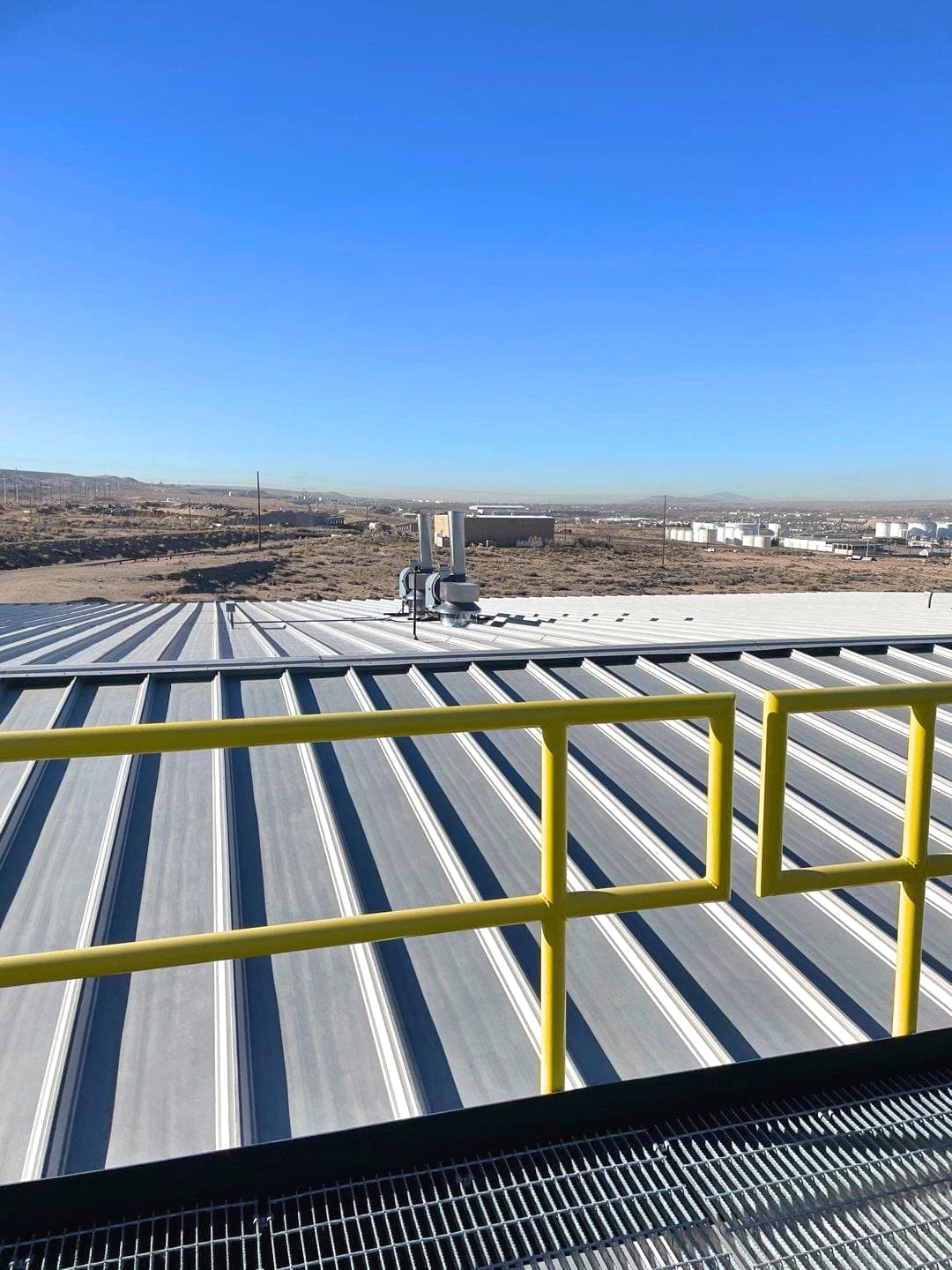 A silver standing-seam commercial metal roof with safety railing and rooftop access, serviced by Paramount Roofing