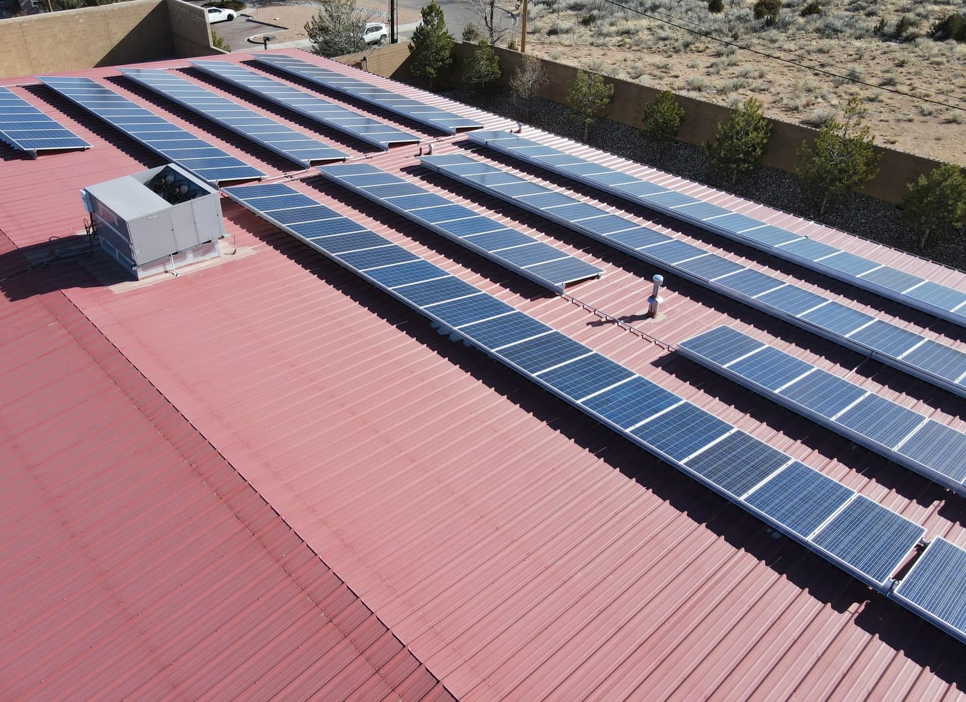 Aerial view of a red standing-seam commercial metal roof lined with solar panels, maintained by Paramount Roofing in New Mexico