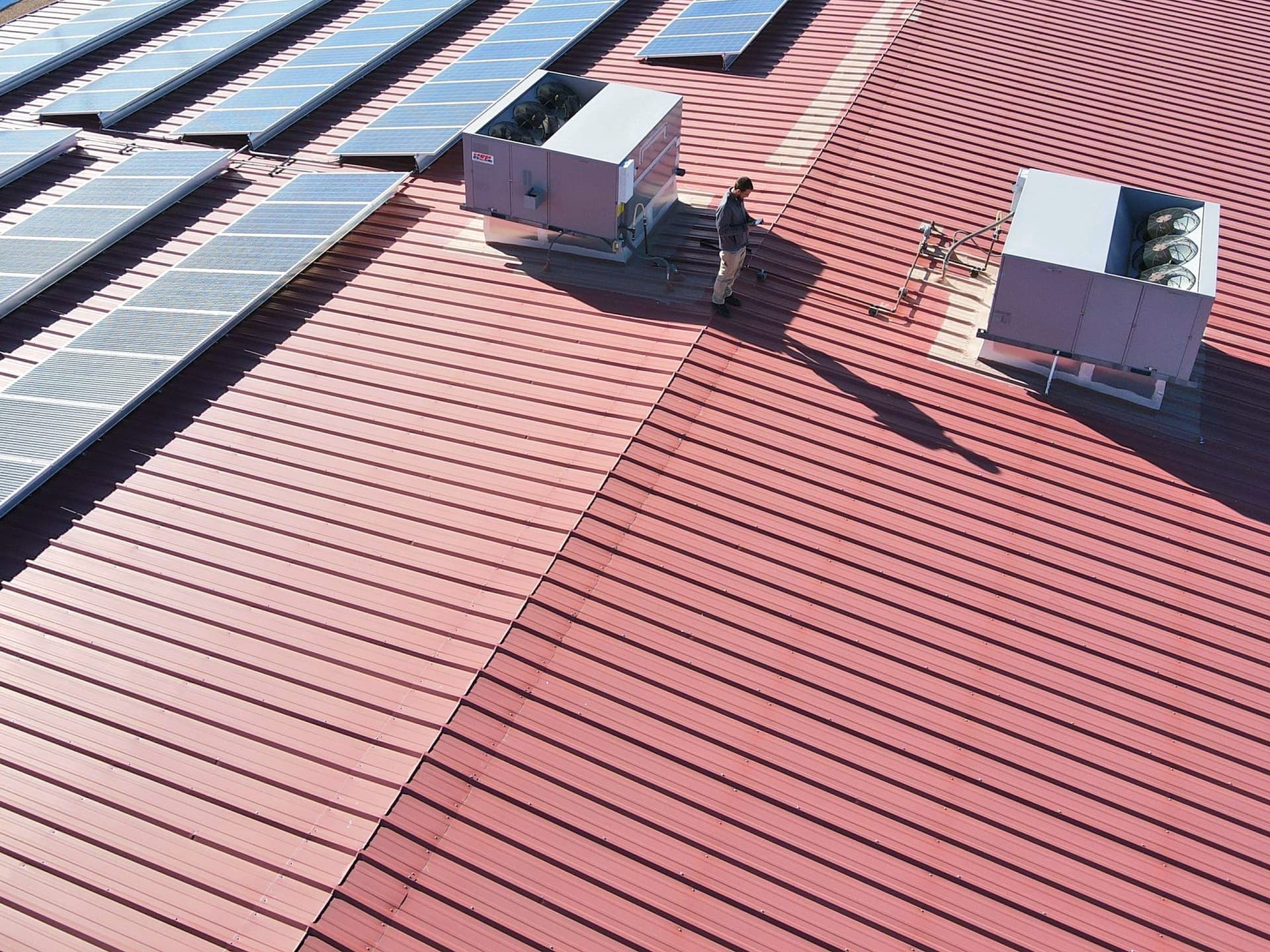 A red standing-seam commercial metal roof with solar panels and rooftop HVAC units, serviced by Paramount Roofing